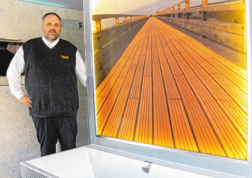 Jan-Dirk Haskamp stellt ein Bad vor, auf dessen Rückseite ein beleuchtetes Bild der Heiligenhafener Seebrücke zu sehen ist. FOTO: BG